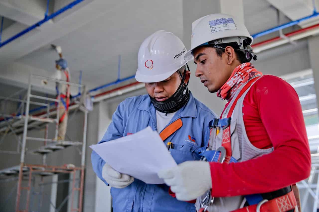 services-04 Two engineers in safety helmets reviewing construction plans at a worksite.